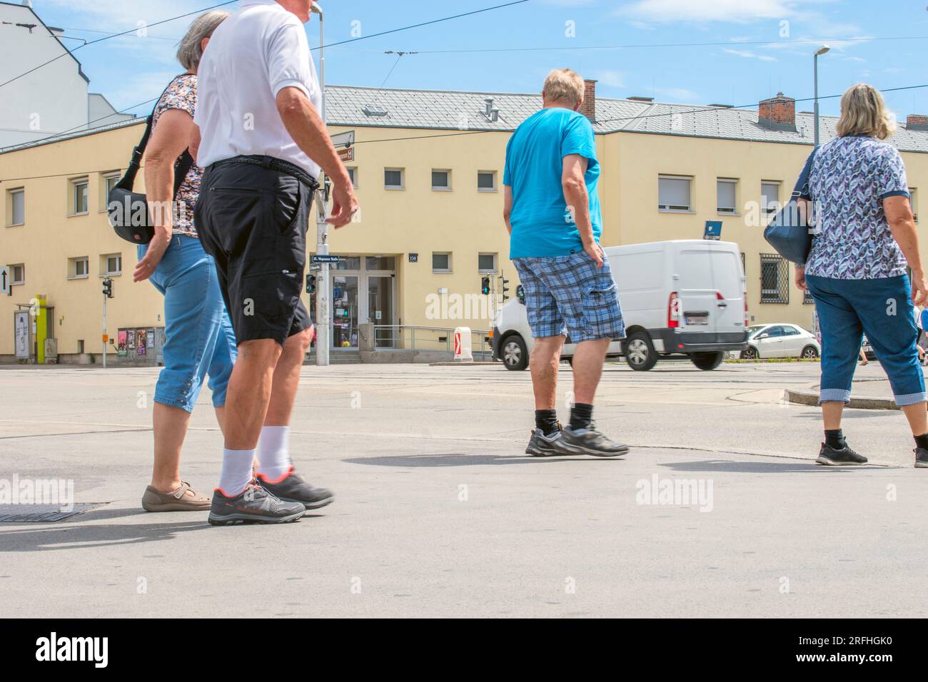 Crosswalk: In mezzo alle strade soleggiate di Vienna, quattro persone aspettano un crosswalk, desiderosi di attraversare il vivace paesaggio urbano in modo sicuro. Foto Stock