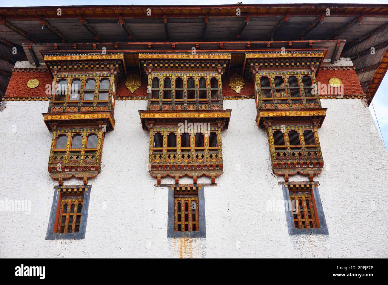 Tre blocchi di tradizionali finestre decorative in legno dipinto a scalpello si estendono dalla parete in pietra bianca di Punakha Dzong nel Regno del Bhutan Foto Stock