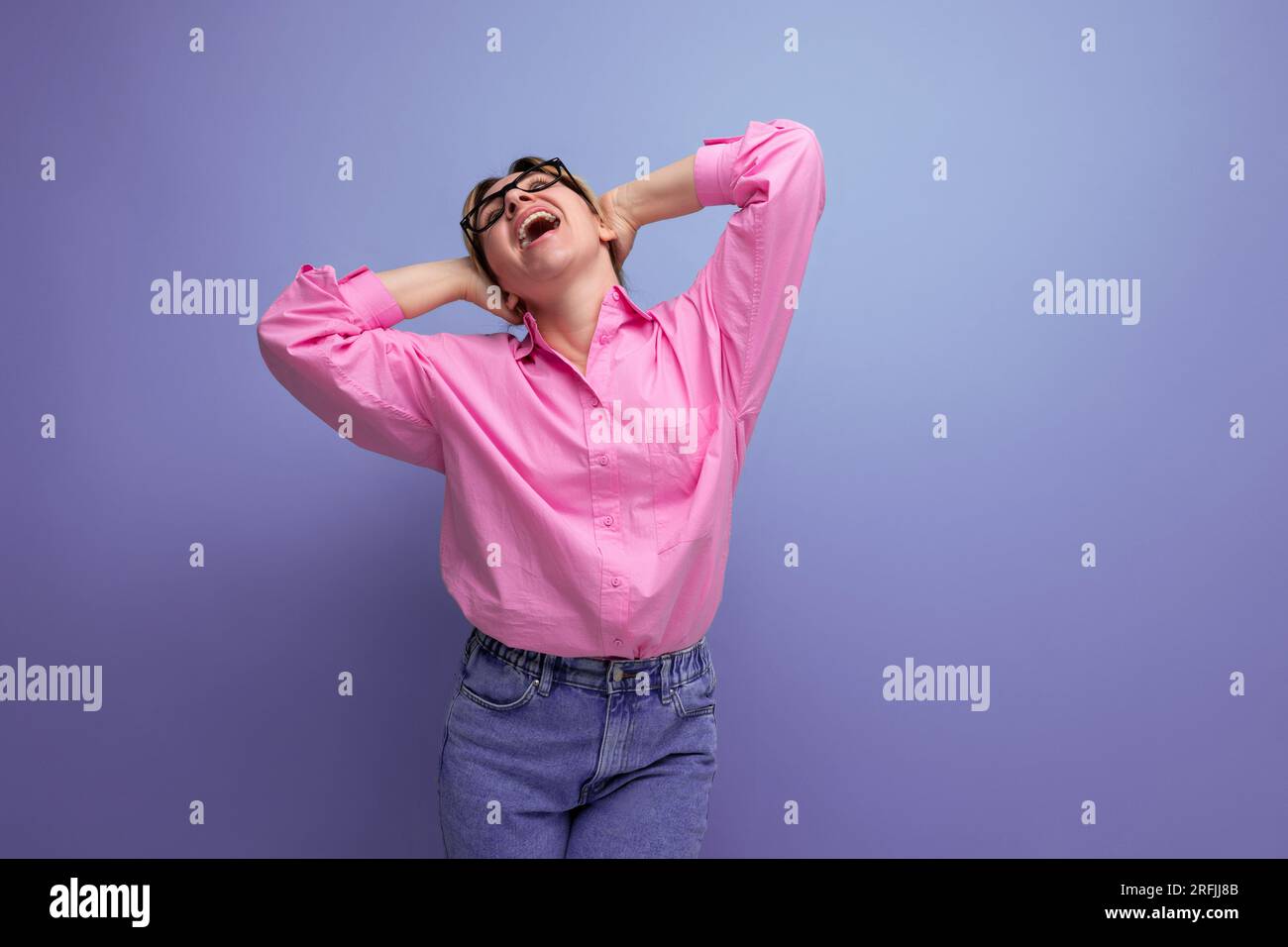 dreamy positivo giovane bionda modello donna caucasica con acconciatura ponytail in look elegante composto da blusa rosa e jeans Foto Stock