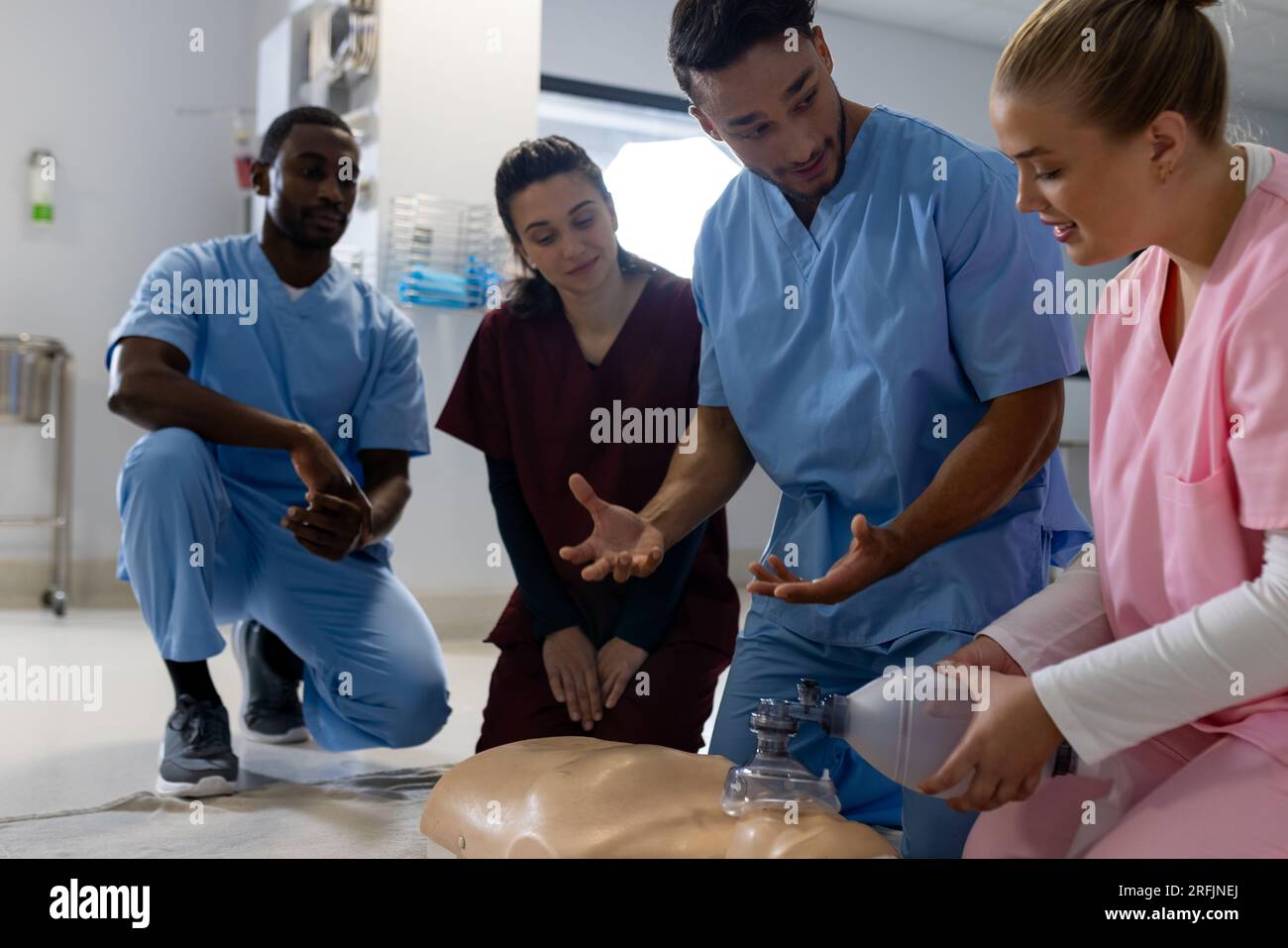 Medico maschio birazziale con diversi medici tirocinanti che imparano rcp su modello in ospedale Foto Stock