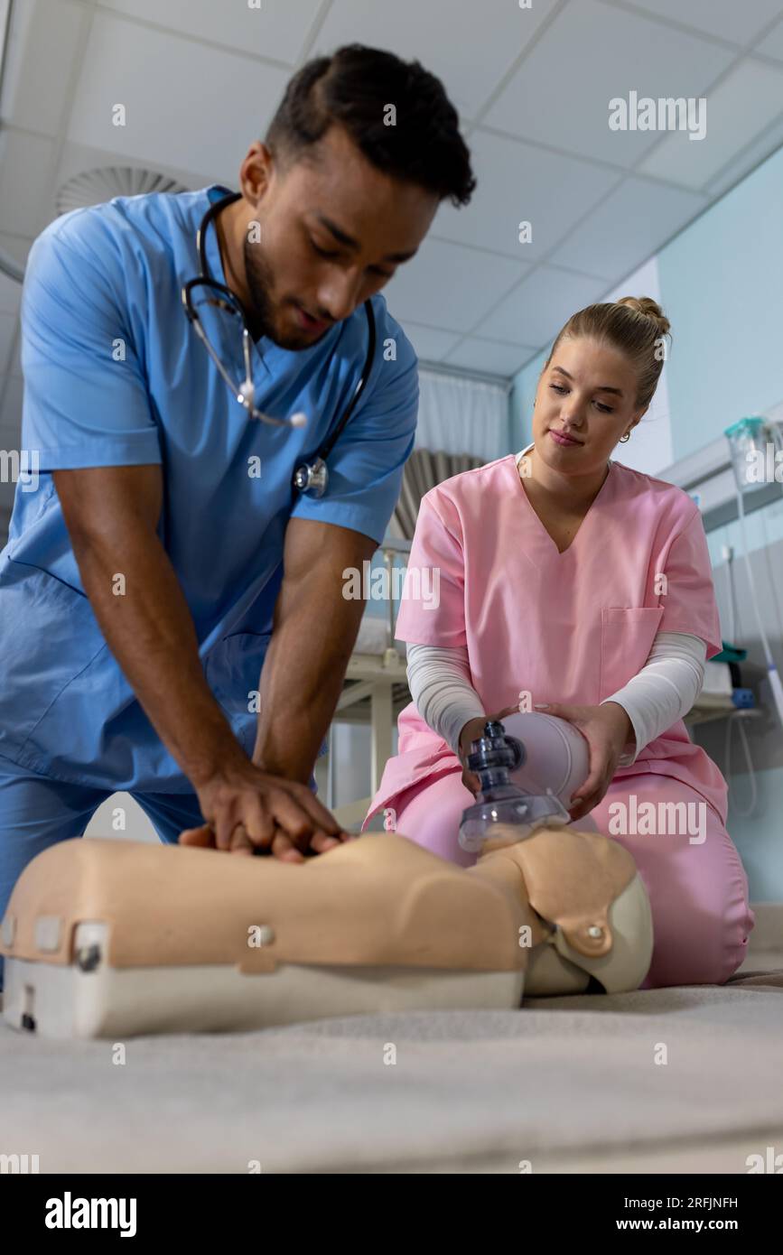 Medico maschio birazziale con diversi medici tirocinanti che imparano rcp su modello in ospedale Foto Stock