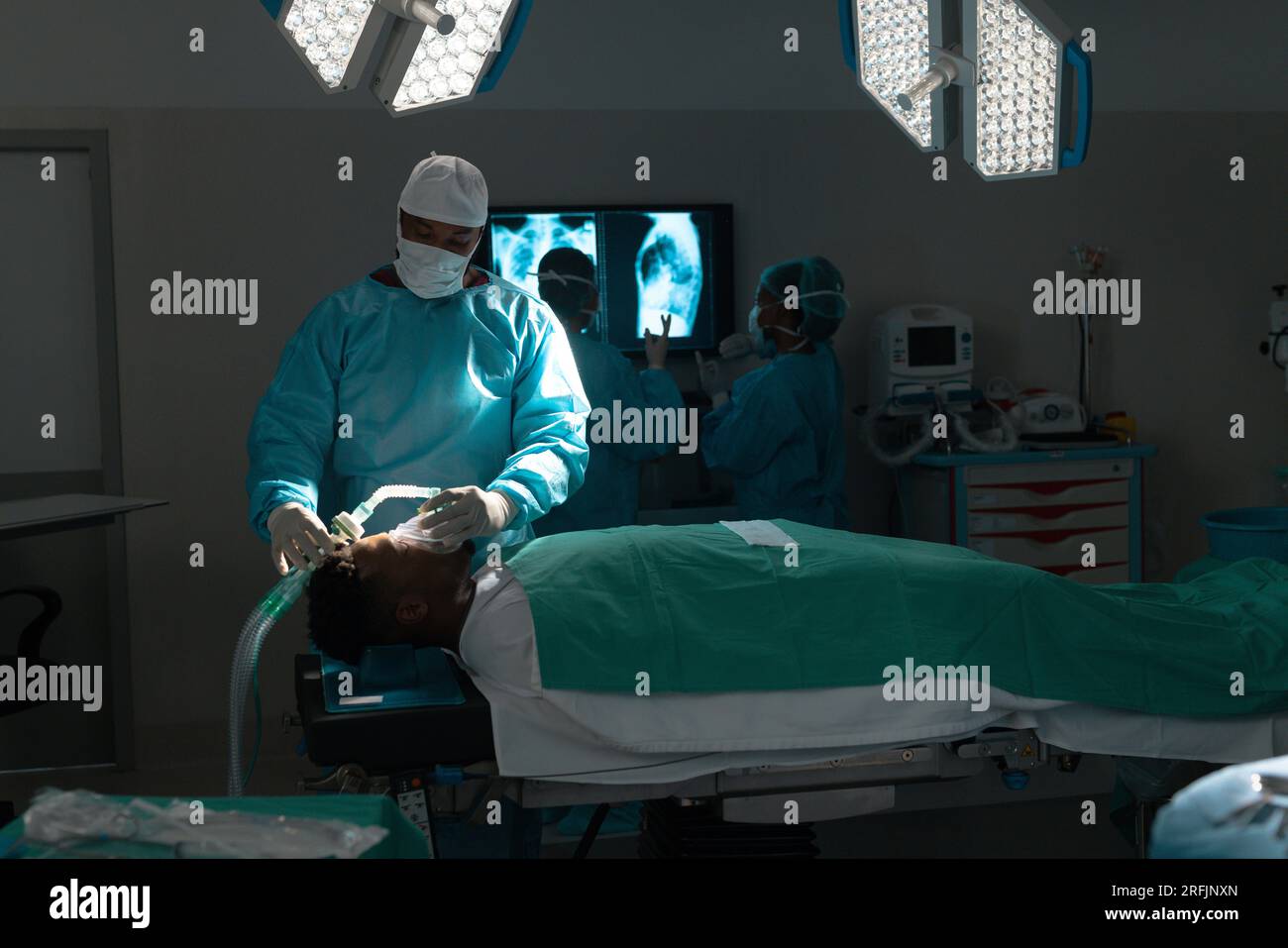 Chirurgo maschio birazziale che pone maschera anestetica sul paziente in sala operatoria all'ospedale Foto Stock