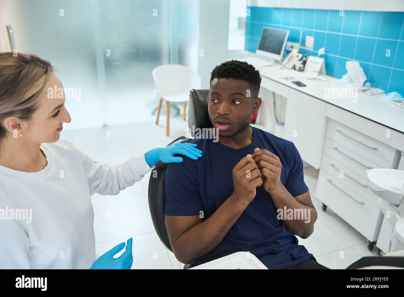 Una donna sorridente dentista che si calmano spaventò un giovane afroamericano che veniva a prendere appuntamento con un medico e sedeva in una sedia dentale Foto Stock