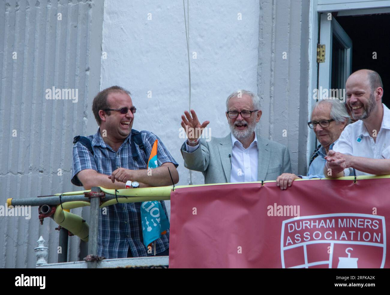 Jeremy Corbyn, Ken Loach e Jamie Driscoll sul balcone del County Hotel che guarda la processione al Miners' Gala Foto Stock