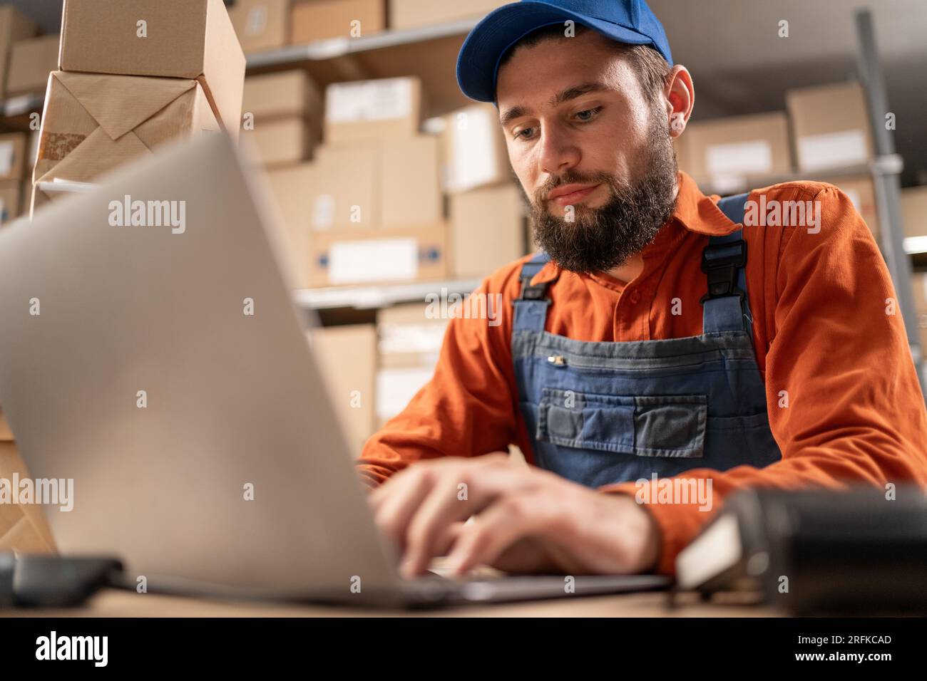 Warehouse worker con laptop che inserisce i dati di inventario nel database che lavora al tavolo, primo piano. POV Foto Stock