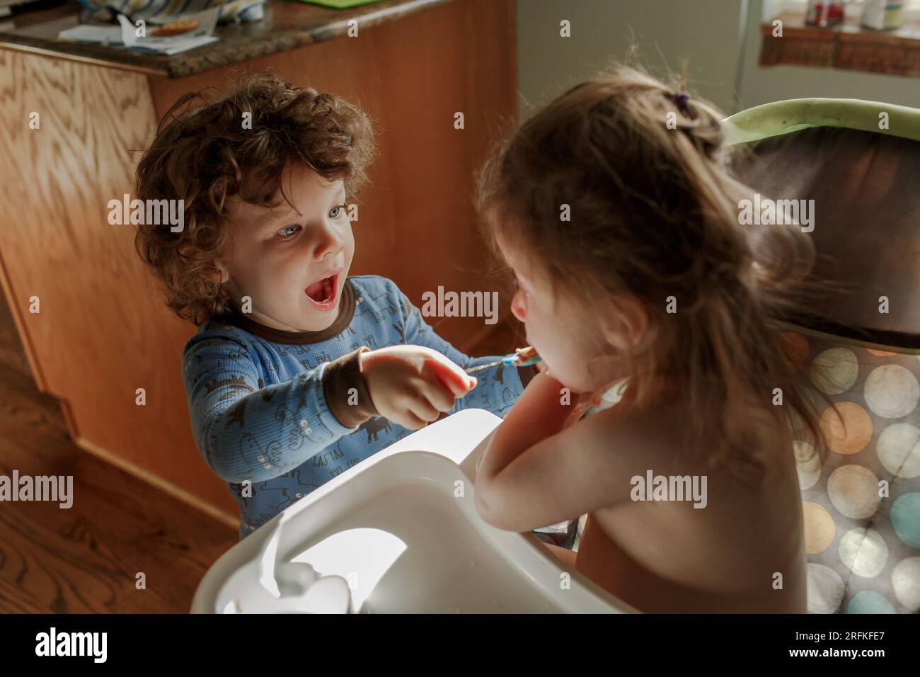 Fratello che dà da mangiare alla sorella in seggiolone Foto Stock