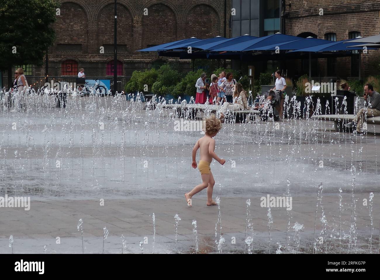 I bambini piccoli si divertono a correre attraverso le fontane danzanti e i getti d'acqua di Granary Square, il cuore della rinata King's Cross, Londra. Foto Stock