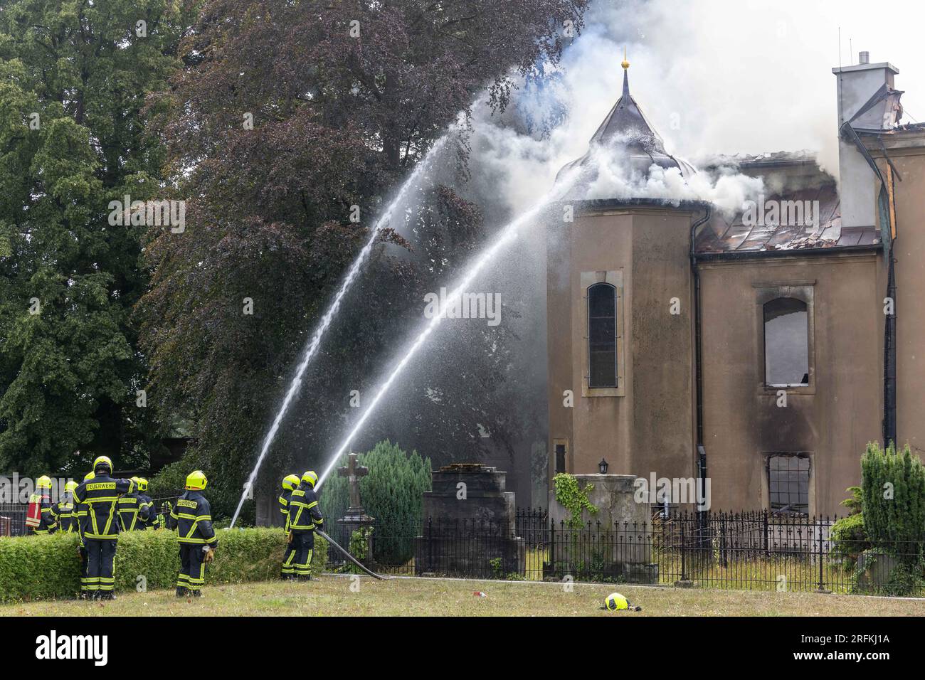 4 agosto 2023, Sassonia, Großröhrsdorf: Il fumo sul lato dell'ala della chiesa di Großröhrsdorf è diventato di nuovo più forte, così i vigili del fuoco hanno immediatamente raffreddato il tetto con acqua e sono stati in grado di evitare che l'incendio scoppiasse di nuovo a questo punto. La chiesa cittadina protestante nella città sassone di Großröhrsdorf è stata distrutta in gran parte da un incendio. Foto: Daniel Schäfer/dpa-Zentralbild/dpa Foto Stock