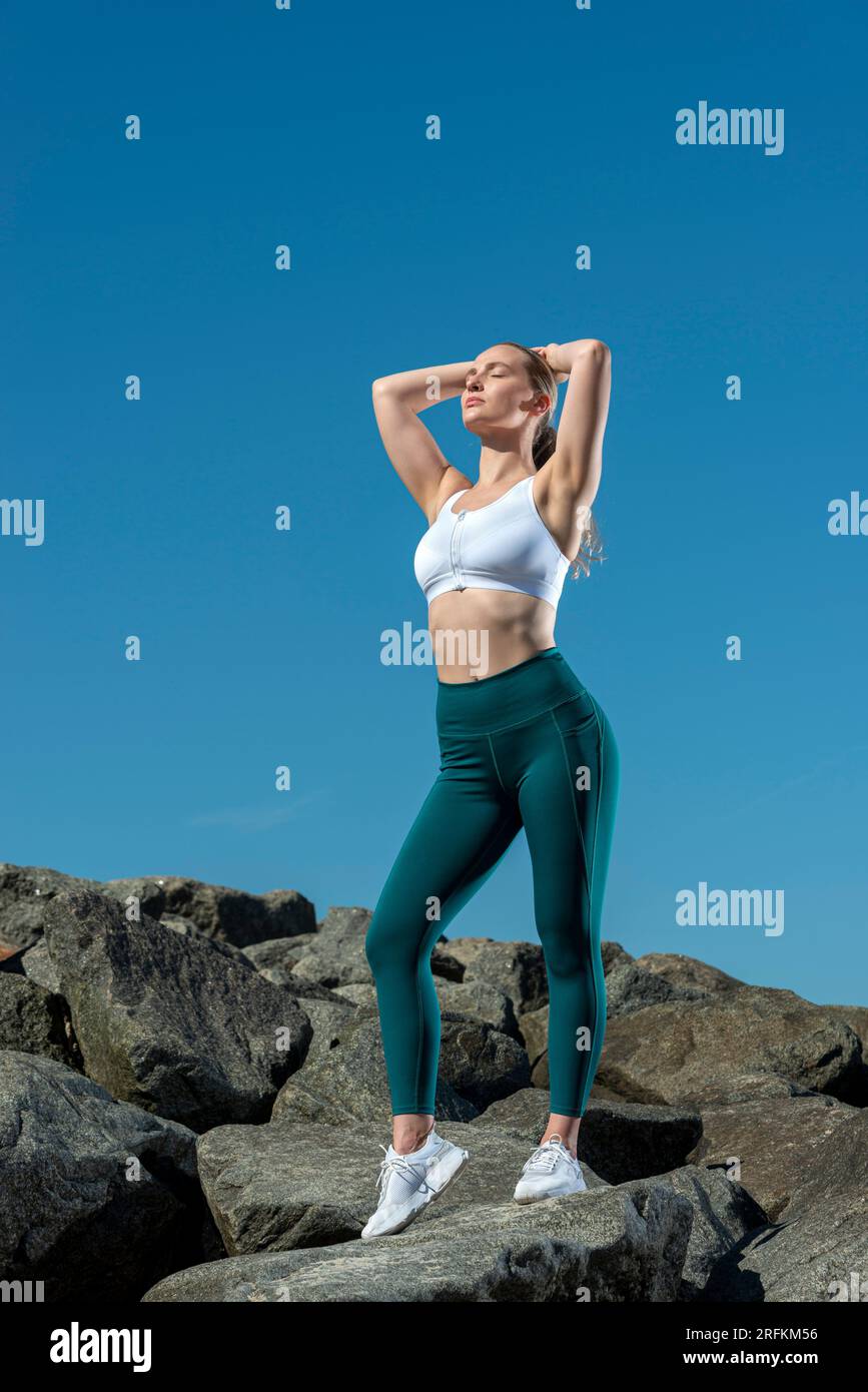 Donna sportiva con le mani sulla testa che si allunga, fa esercizio all'aperto sotto il sole Foto Stock
