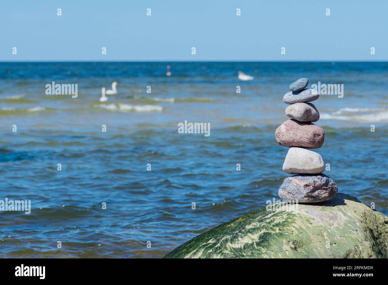 Bilanciare pietre su una grande roccia con erba marina sulla spiaggia, con onde blu sullo sfondo, Mar Baltico, Olando Kepure, Lituania Foto Stock