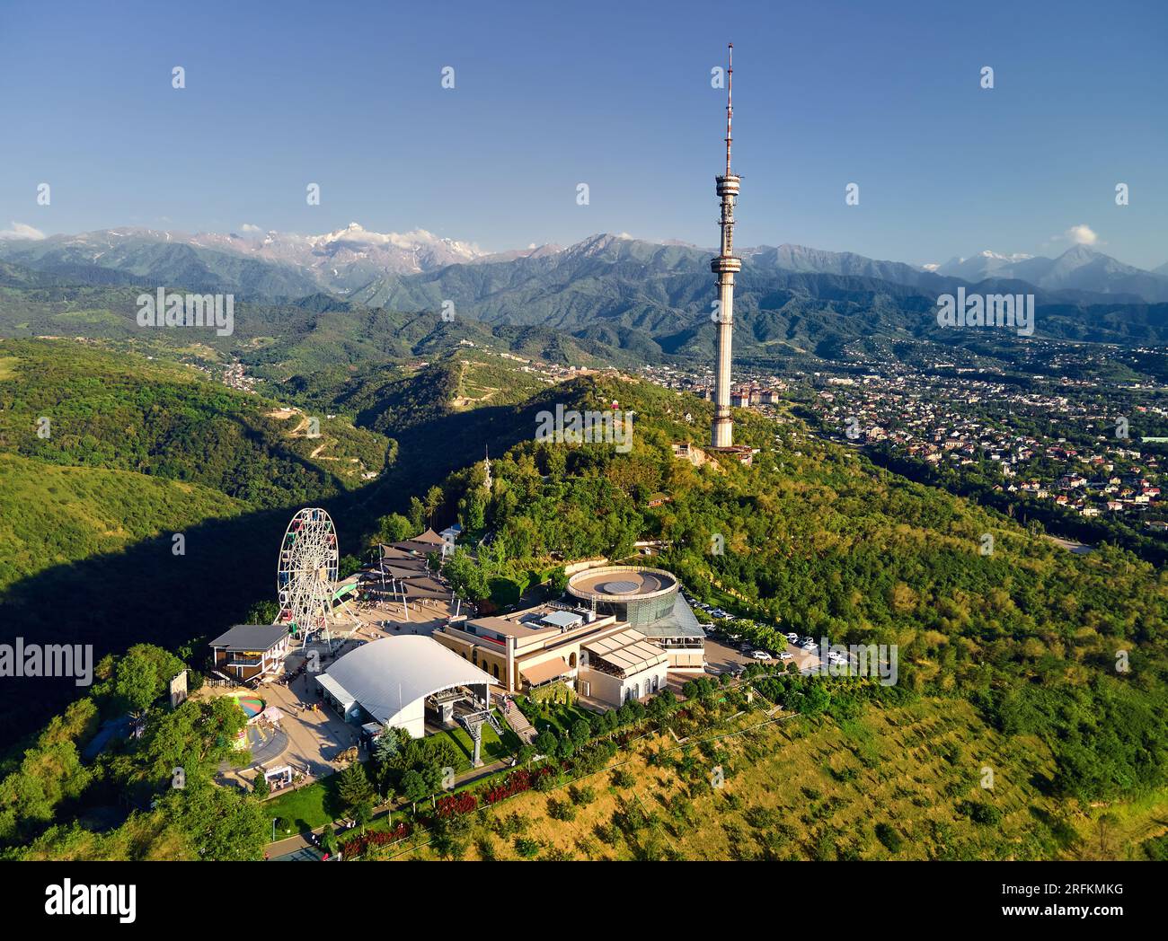Foto aerea con drone del parco collinare di Koktobe con ruota panoramica, un simbolo dell'alta torre televisiva di Almaty, contro le montagne innevate in Kazakistan Foto Stock