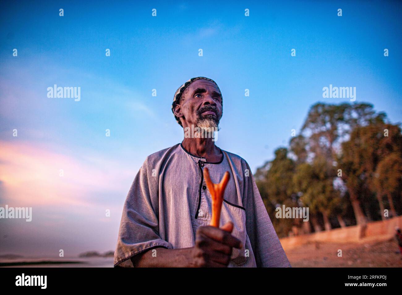 Tramonto con un narratore africano più anziano che tiene in mano un bastone da passeggio, foto sincera di persone africane reali in un ambiente naturale. Mopti, Mali, Afric Occidentale Foto Stock