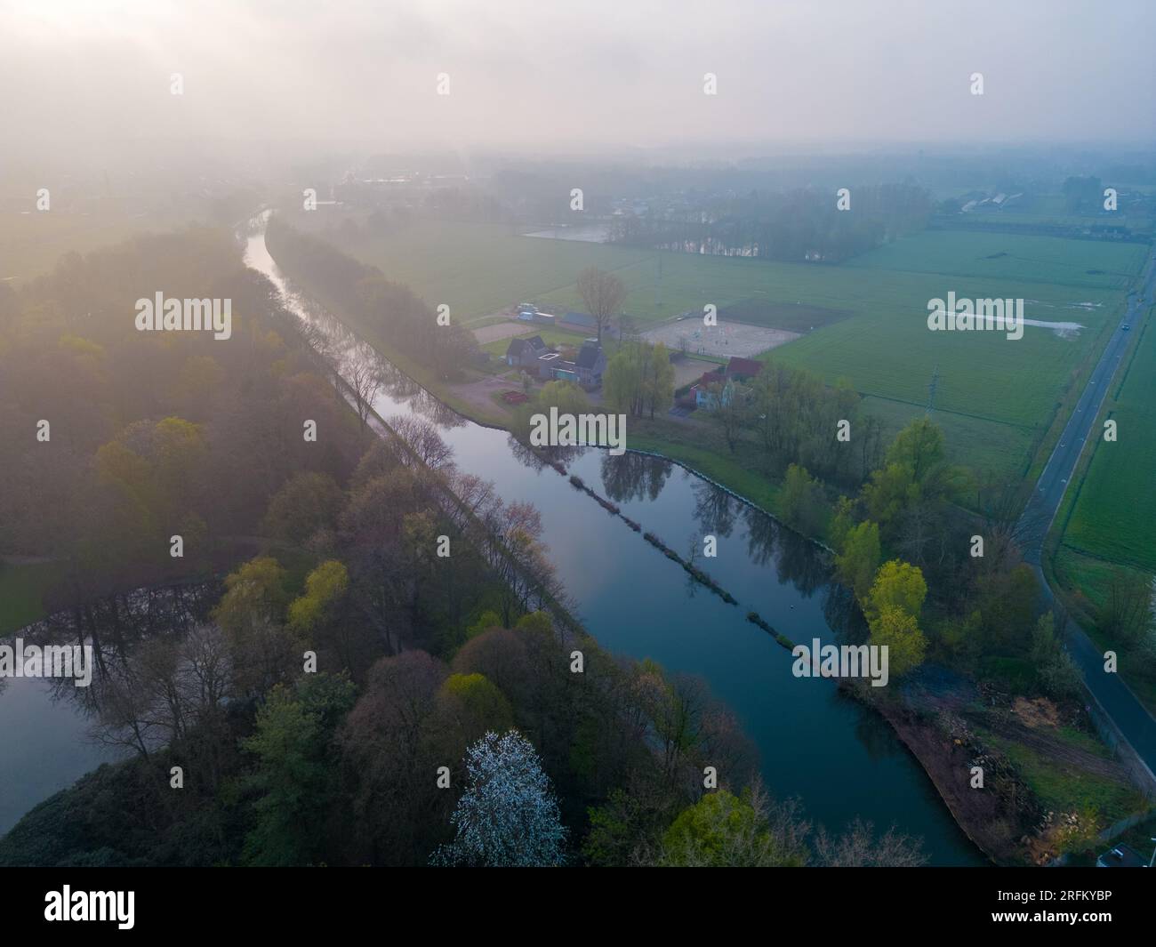Immergiti nell'incantevole bellezza di una mistica mattinata mentre la fotocamera ti inquadra in un'accattivante vista aerea di un fiume, di un campo agricolo e di un paesaggio forestale. Sotto il dolce abbraccio della nebbia mattutina, il fiume sereno si snoda attraverso i lussureggianti campi verdi della fattoria e la maestosa foresta. Quando il sole sorge, i suoi raggi dorati penetrano attraverso la nebbia, gettando un bagliore caldo ed etereo sul paesaggio. Questa panoramica cattura l'essenza della tranquillità e il fascino del risveglio della natura. Scopri la bellezza serena e l'atmosfera accattivante di questa magica scena mattutina, dove l'interazione della nebbia Foto Stock