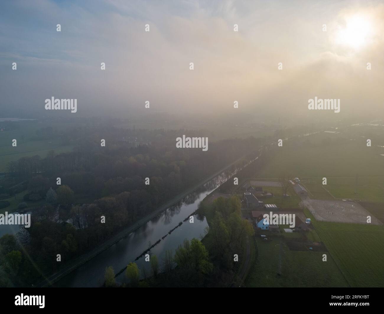 Immergiti nell'incantevole bellezza di una mistica mattinata mentre la fotocamera ti inquadra in un'accattivante vista aerea di un fiume, di un campo agricolo e di un paesaggio forestale. Sotto il dolce abbraccio della nebbia mattutina, il fiume sereno si snoda attraverso i lussureggianti campi verdi della fattoria e la maestosa foresta. Quando il sole sorge, i suoi raggi dorati penetrano attraverso la nebbia, gettando un bagliore caldo ed etereo sul paesaggio. Questa panoramica cattura l'essenza della tranquillità e il fascino del risveglio della natura. Scopri la bellezza serena e l'atmosfera accattivante di questa magica scena mattutina, dove l'interazione della nebbia Foto Stock