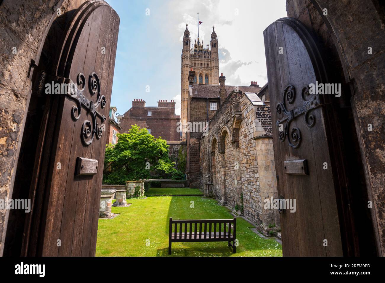 Guarda attraverso vecchie porte medievali in legno e l'arco in uno storico cortile in mattoni con il Palazzo di Westminster, la Victoria Tower del Parlamento britannico. Foto Stock
