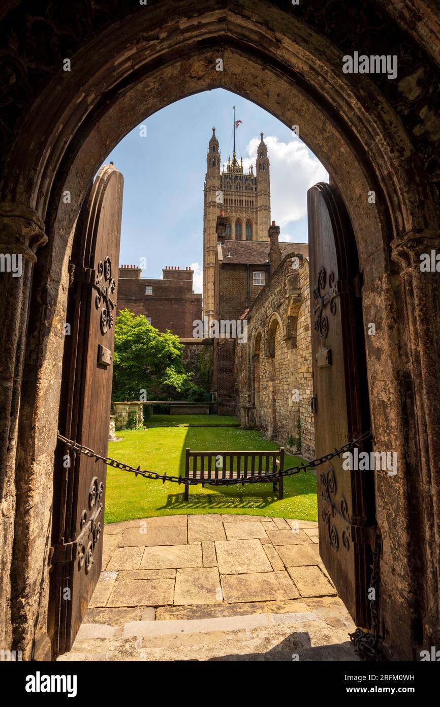 Guarda attraverso vecchie porte medievali in legno e l'arco in uno storico cortile in mattoni con il Palazzo di Westminster, la Victoria Tower del Parlamento britannico. Foto Stock