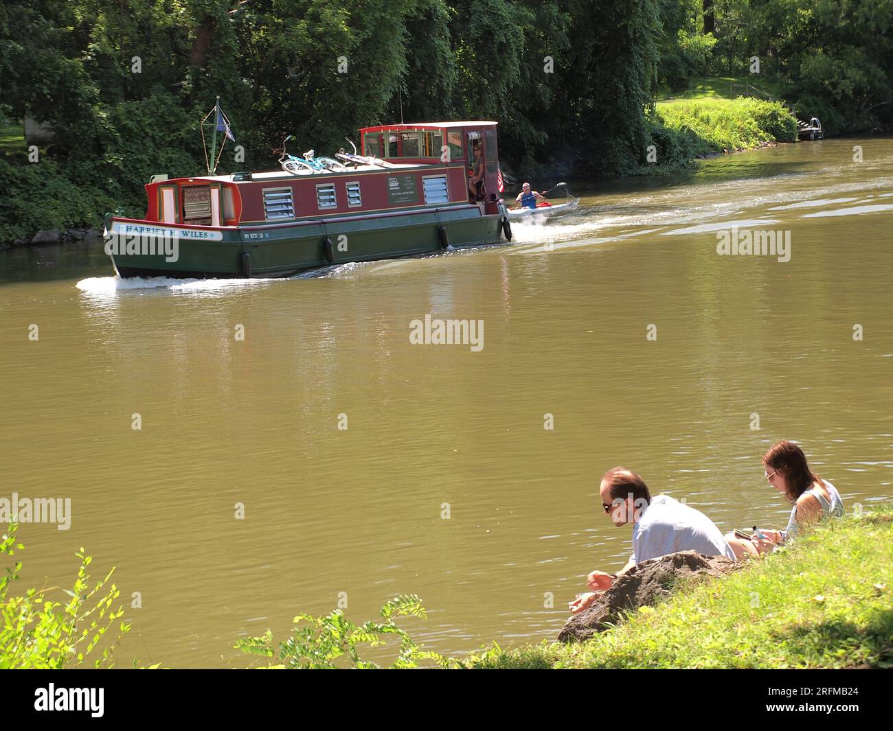 Barca sul canale di Erie con due persone sedute sulla riva del fiume a guardare. Foto Stock