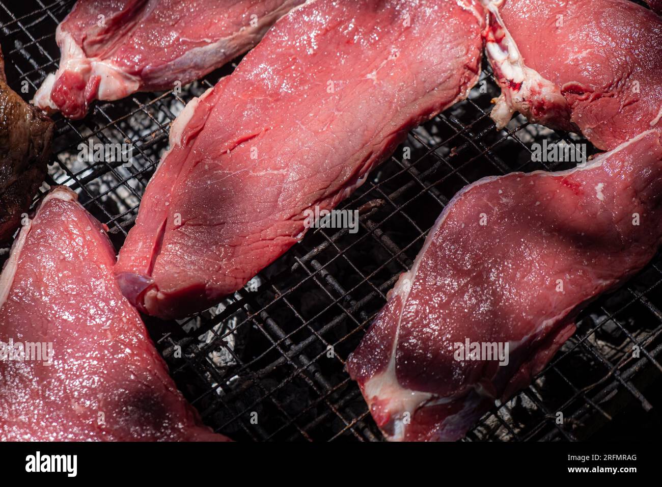 pezzi di manzo crudo preparati per la cottura alla griglia su una griglia a carbone Foto Stock