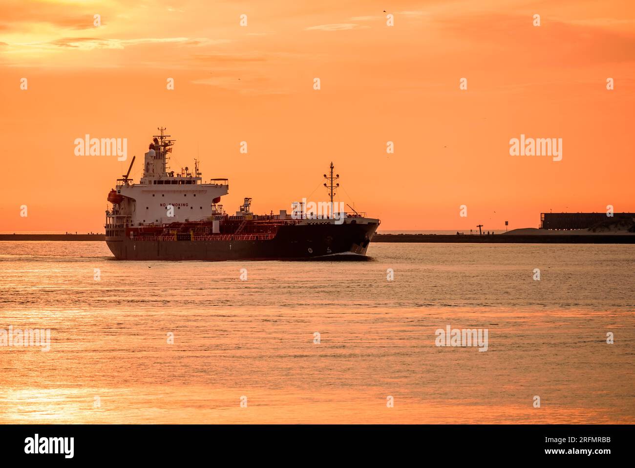 Tramonto estivo arancione su una petroliera che entra in un porto marittimo Foto Stock