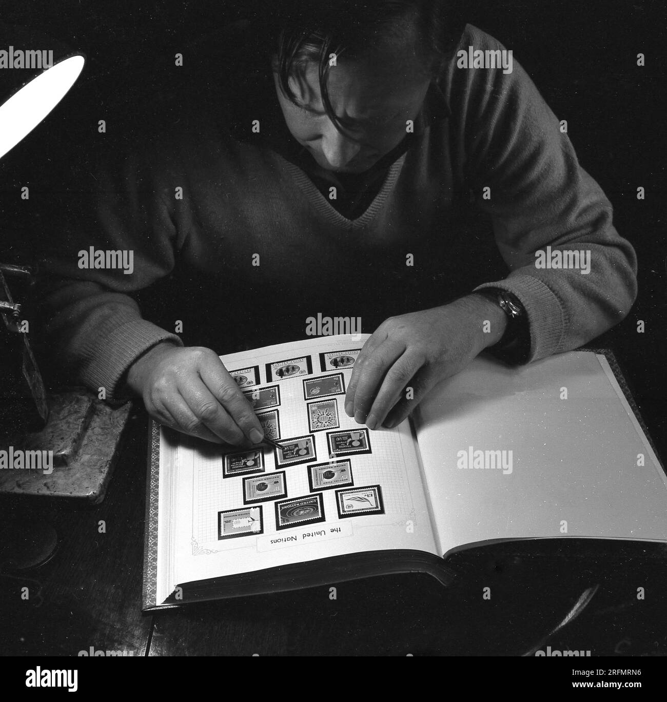 1969, storico, un uomo che mette con cura un francobollo emesso dalle Nazioni Unite nel suo album di francobolli su una pagina intitolata, The United Nations, England, UK. Foto Stock