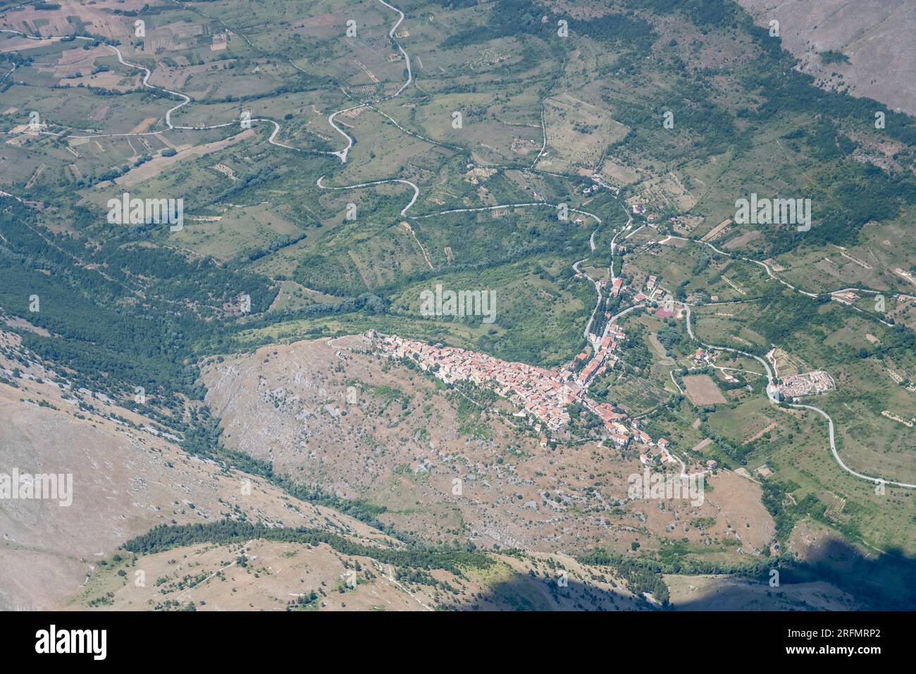 Paesaggio aereo, da un aliante, con villaggio di montagna nella verde valle, girato da sud-ovest in una luminosa luce estiva a Ortona de Marsi, Apennin Foto Stock
