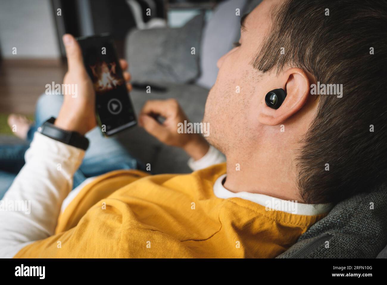 un giovane bellissimo uomo guarda un film sul suo smartphone. Visualizzazione di videoclip su Internet da parte di un utente. Ascolto di musica tramite telefono. Foto Stock