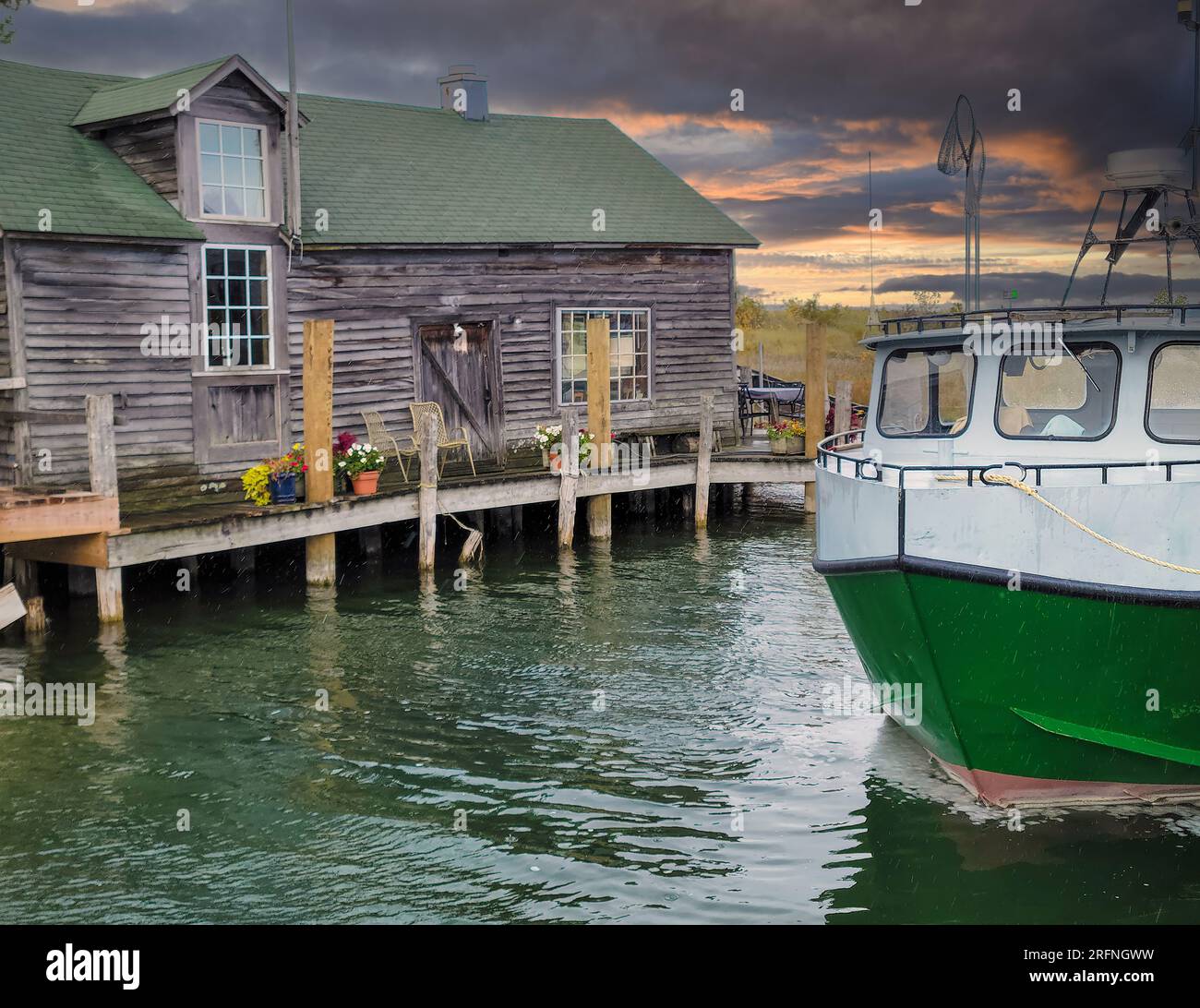 Vecchia cabina rustica con una barca verde e bianca in un canale e gocce di pioggia Foto Stock