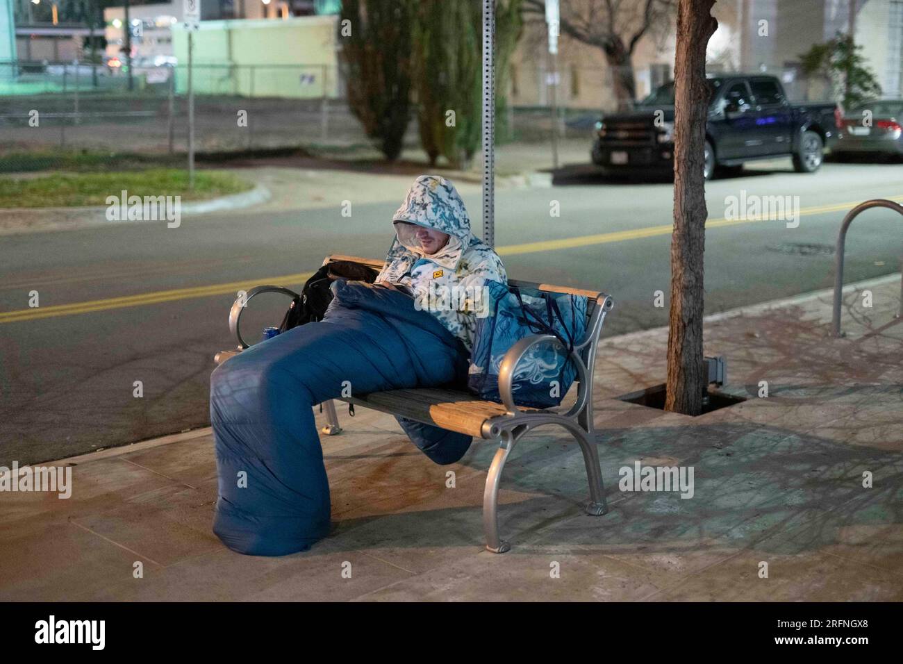 Un uomo che vive per strada guarda un cellulare mentre cerca di tenersi al caldo nel centro di Austin in una fredda notte di gennaio nel Texas centrale. ©Bob Daemmrich Foto Stock