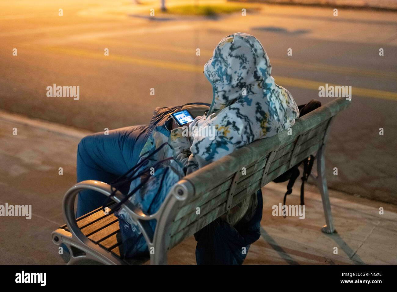 Un uomo che vive per strada guarda un cellulare mentre cerca di tenersi al caldo nel centro di Austin in una fredda notte di gennaio nel Texas centrale. ©Bob Daemmrich Foto Stock
