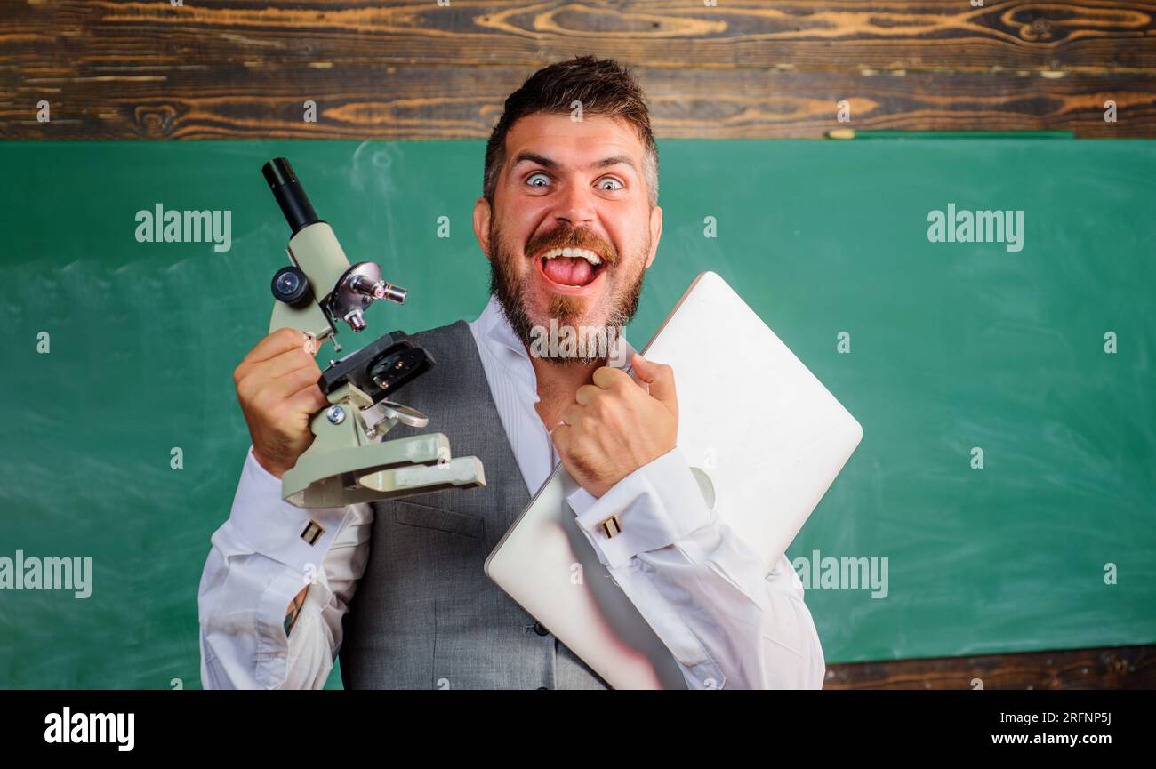 Allievo o insegnante felice con laptop e microscopio in classe. Uomo barbuto con notebook e microscopio. Lezione di biologia o chimica. Istruzione Foto Stock