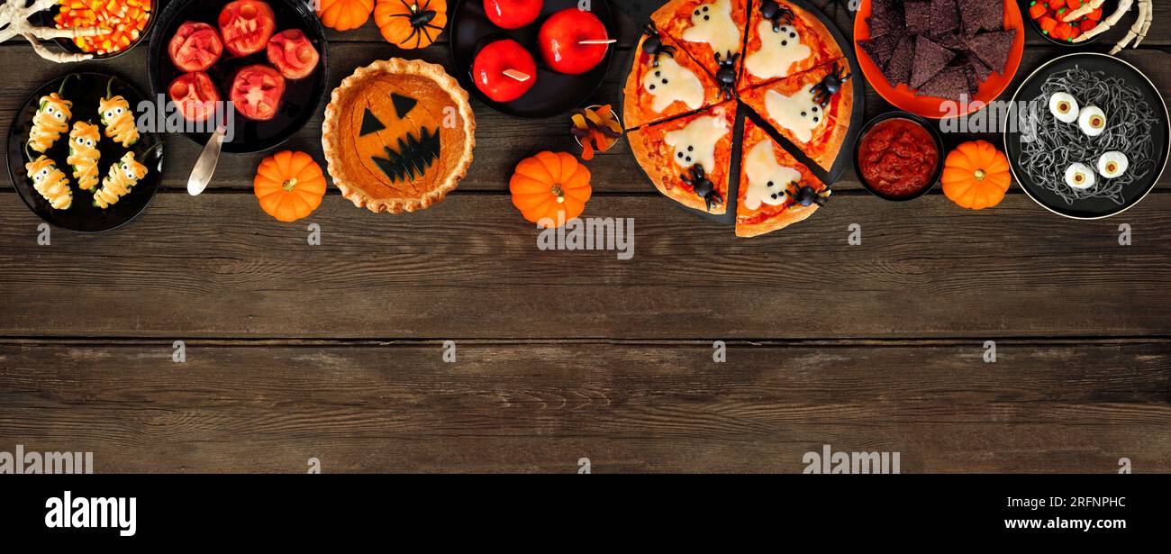 Divertente cena di Halloween con bordo superiore su uno sfondo banner di legno scuro. Vista dall'alto. Pizza, torta di zucca jack o lantern, mele caramelle, spag di bulbi oculari Foto Stock