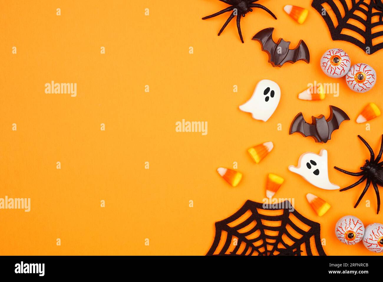 Bordo laterale di Halloween con caramelle sparse e decorazioni. Vista dall'alto su uno sfondo arancione con spazio per la copia. Foto Stock