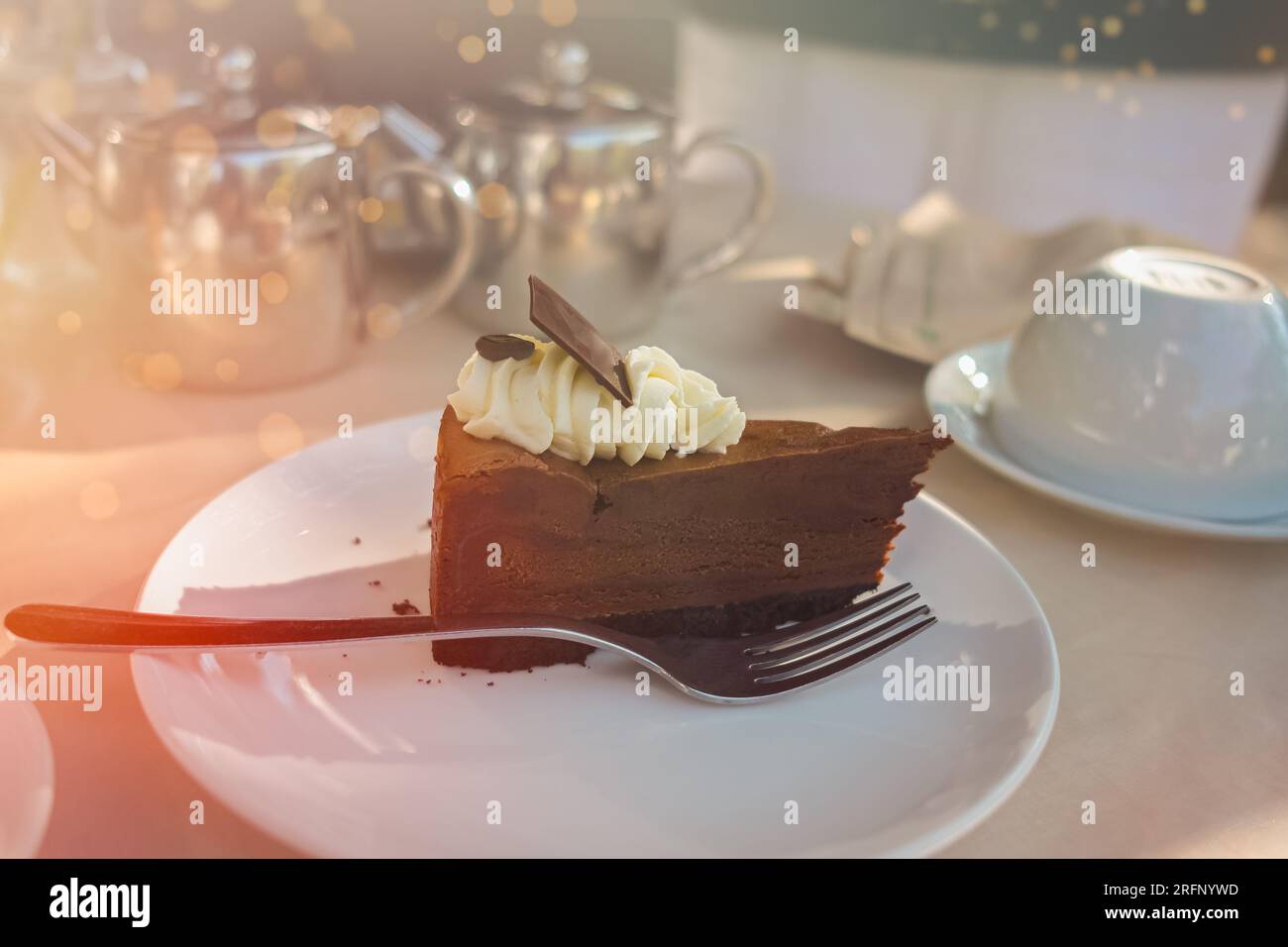 Cheesecake al cioccolato con panna sul tavolo bianco. Fetta di cheesecake al cioccolato sul piatto, natura morta con sfondo chiaro. Snack o caffè gustosi Foto Stock