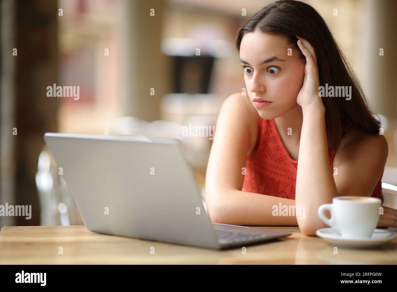 Donna scioccata che guarda i contenuti del notebook in una terrazza del bar Foto Stock