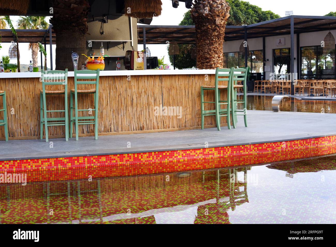 Tropic bar vicino alla piscina in un giorno d'estate con palme sullo sfondo. Riflesso sull'acqua e sulle sedie. Foto Stock