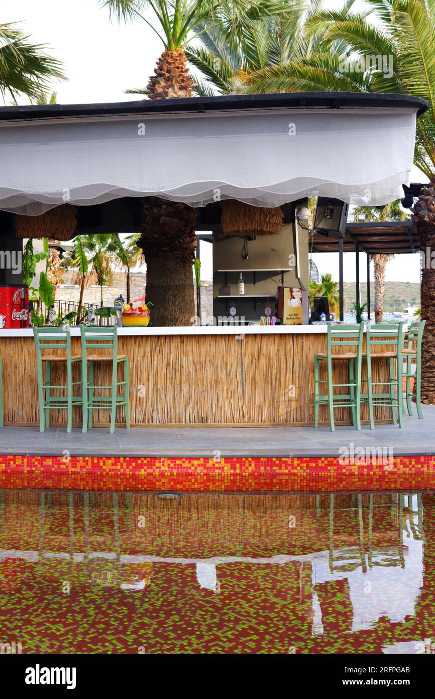 Tropic bar vicino alla piscina in un giorno d'estate con palme sullo sfondo. Riflesso sull'acqua e sulle sedie. Foto Stock