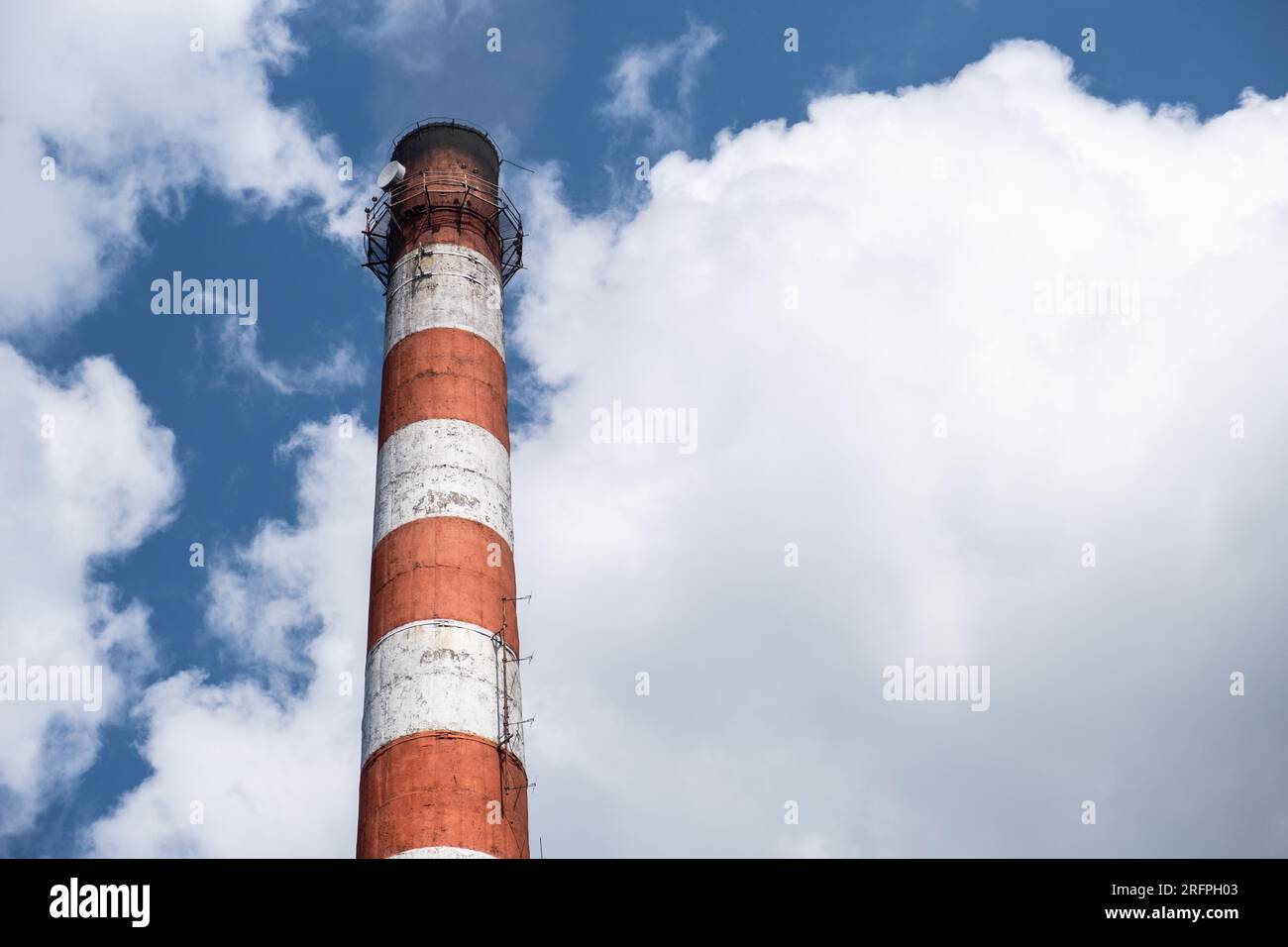 Un alto camino rosso-bianco di una sala caldaia contro le nuvole blu del cielo. Foto Stock