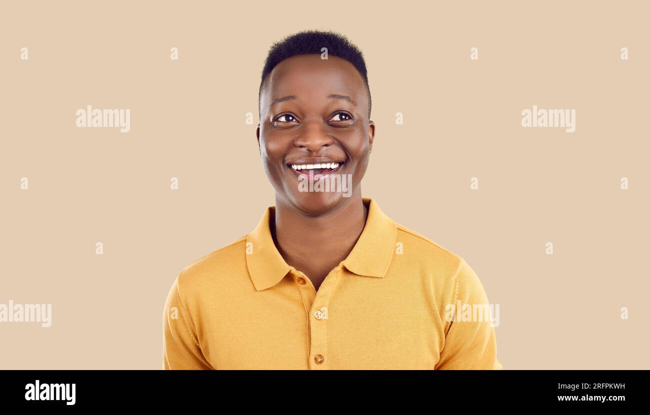Ritratto di un giovane indiano africano allegro e divertente che guarda da parte su sfondo beige. Foto Stock