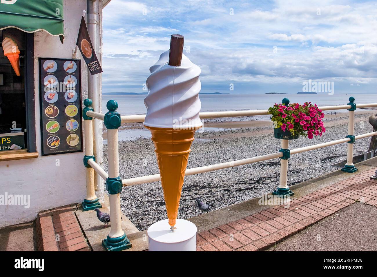 Un gigantesco cono gelato di plastica sul lungomare in un pomeriggio nuvoloso. Signor Whippy. Fiori. Pavimentazione. 99 Flake. Foto Stock