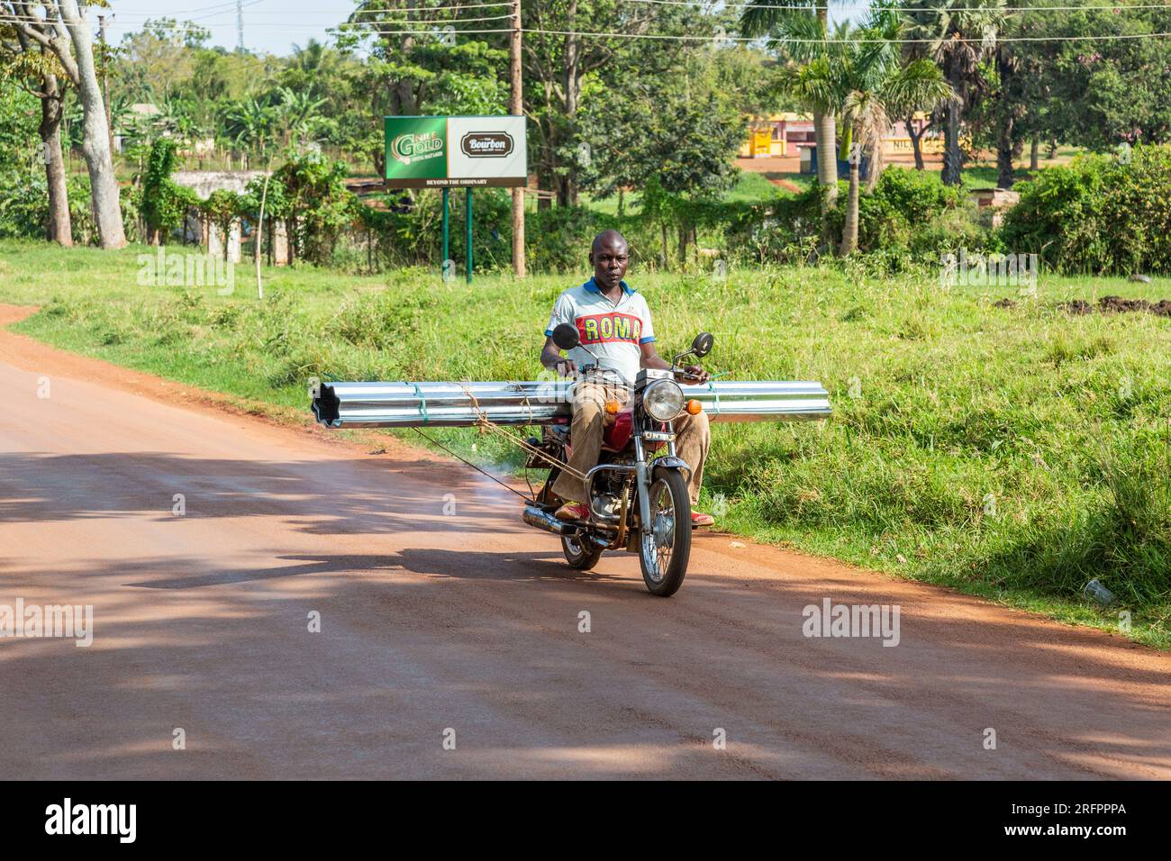 Motociclista su una strada vicino a Jinja, che trasporta lunghi tubi metallici attraverso il suo veicolo. Foto Stock