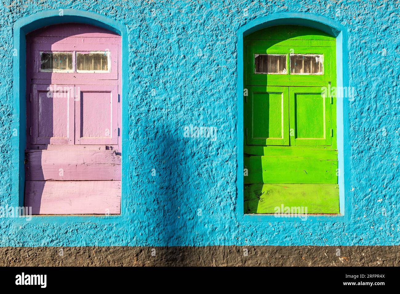 Due finestre francesi, una rosa, l'altra verde, su un muro blu. Colori audaci. Foto Stock