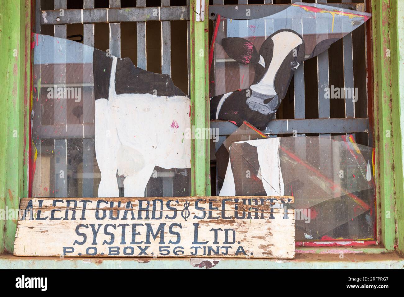 Vetrina rotta di un installatore di sistemi di allarme e sicurezza, decorato con una mucca. Jinja, Uganda. Foto Stock