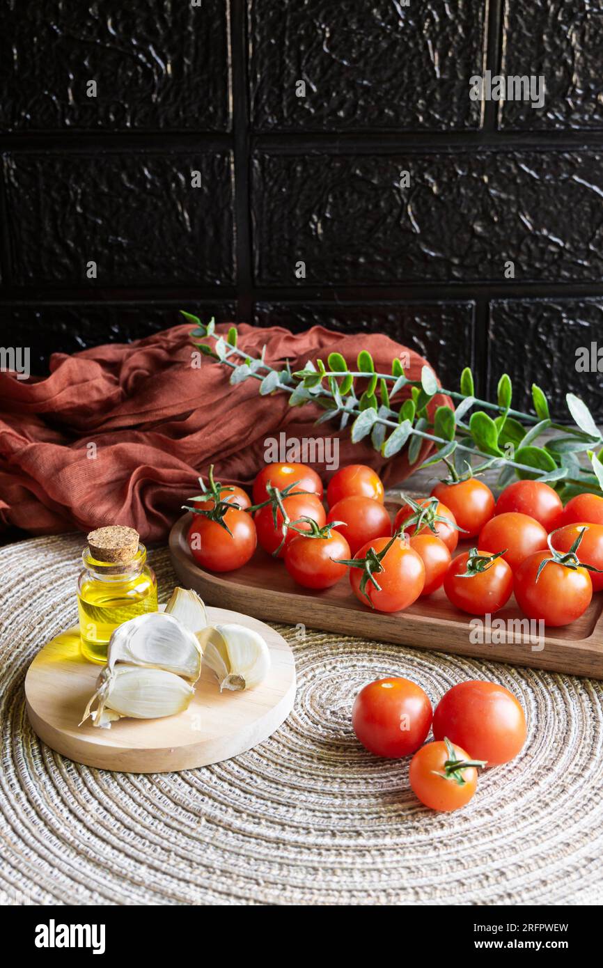 Immagine verticale di un tavolo con prodotti sani. Pomodori ciliegini, olio extravergine di oliva spagnolo e spicchi d'aglio. Foto Stock