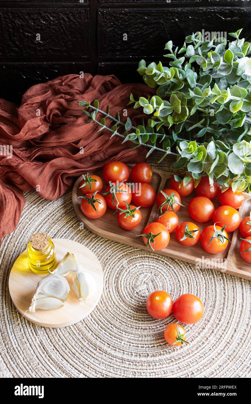 Immagine verticale di un tavolo con prodotti sani. Pomodori ciliegini, olio extravergine di oliva spagnolo e spicchi d'aglio. Foto Stock