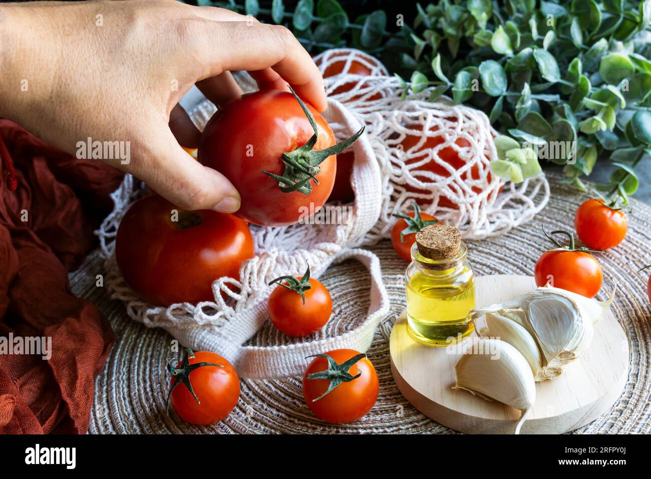 Mano umana che tiene un pomodoro rosso di una tavola con prodotti mediterranei sani. Shot orizzontale. Foto Stock