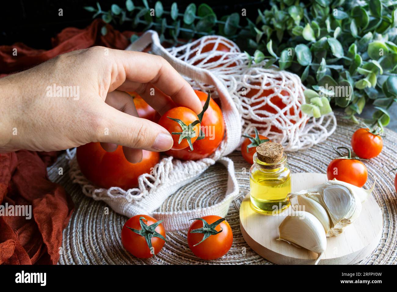 Mano umana che tiene un pomodoro ciliegia di una tavola con prodotti mediterranei sani. Shot orizzontale. Foto Stock