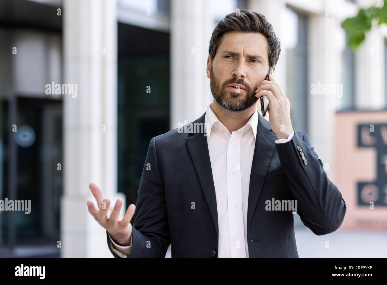 Uomo d'affari preoccupato e serio, in completo accordo e parlando in modo esplicito al telefono, risolvendo problemi e domande. Foto Stock