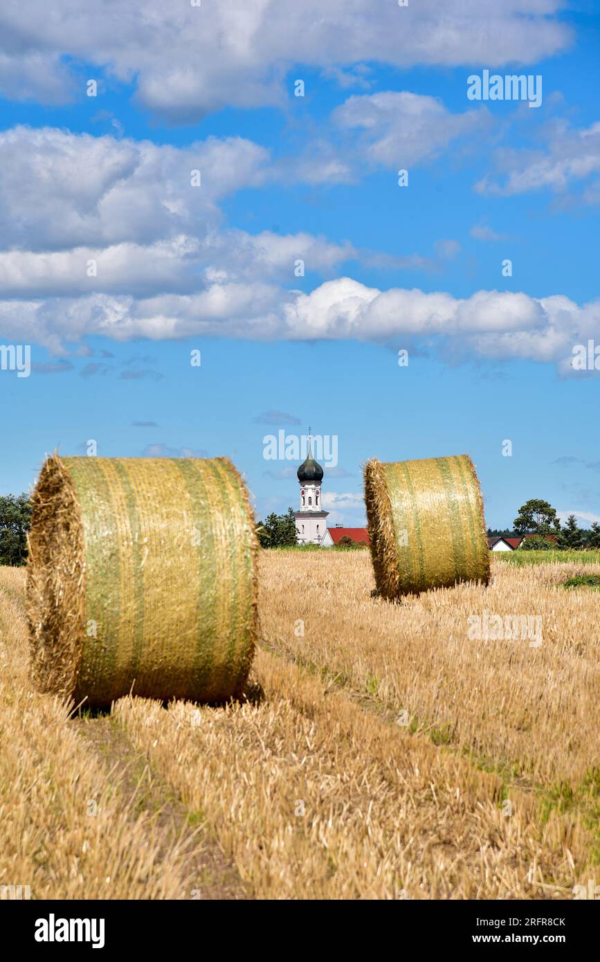 Balle di paglia su un campo di grano raccolto, sullo sfondo la chiesa del villaggio con cupola a cipolla, Baviera, Germania, Europa Foto Stock
