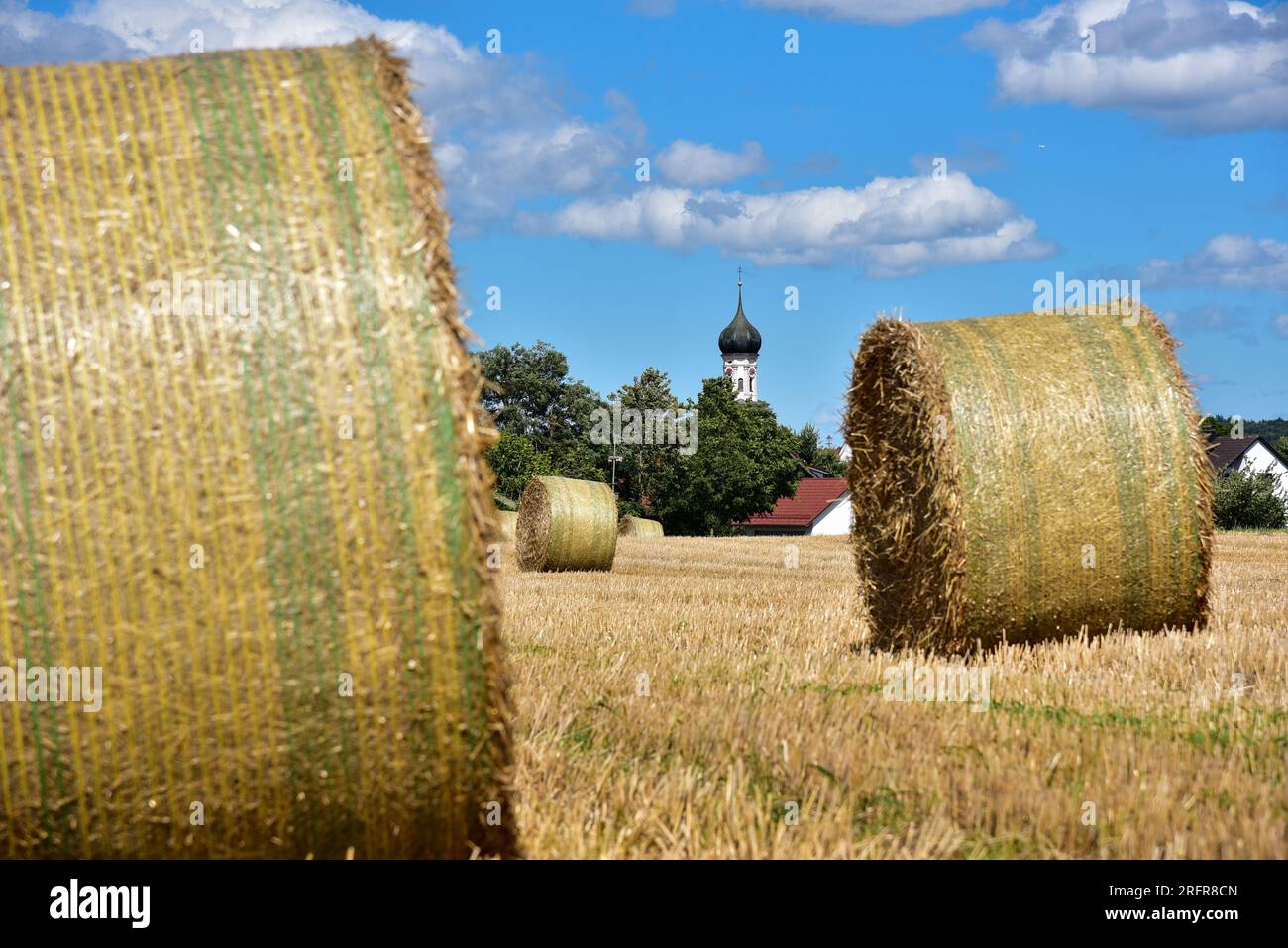 Balle di paglia su un campo di grano raccolto, sullo sfondo la chiesa del villaggio con cupola a cipolla, Baviera, Germania, Europa Foto Stock