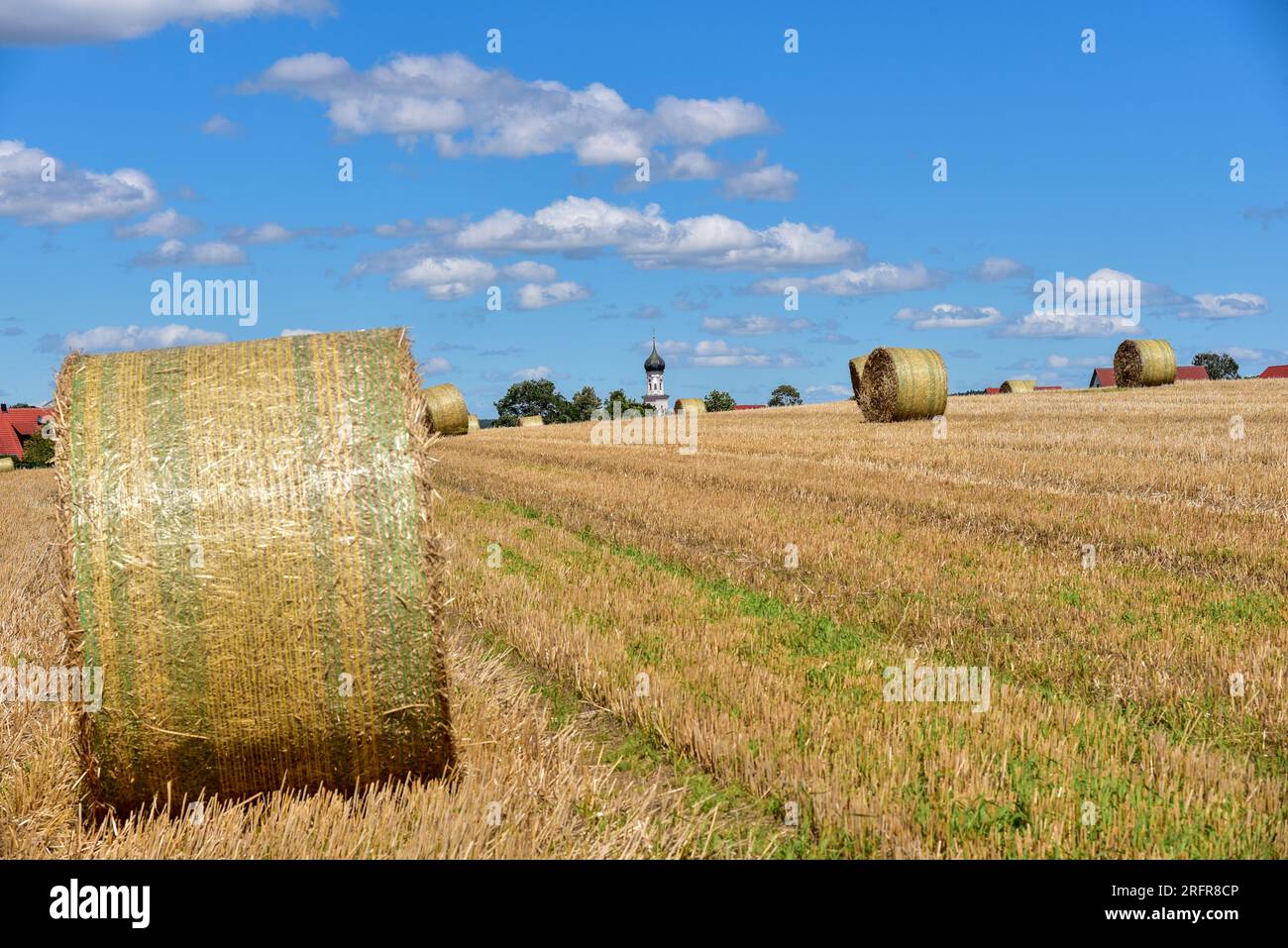 Balle di paglia su un campo di grano raccolto, sullo sfondo la chiesa del villaggio con cupola a cipolla, Baviera, Germania, Europa Foto Stock